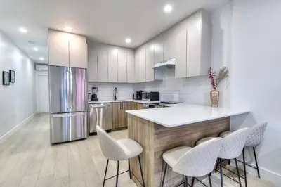 a kitchen with white cabinets and a counter with stools at Montreal's Downtown Glow & Go 2BR Apartment in Montréal