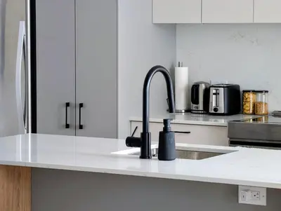 a kitchen with white cabinets and a sink with a faucet at Old Montreal Suite with Rooftop Pool & Terrace in Montréal