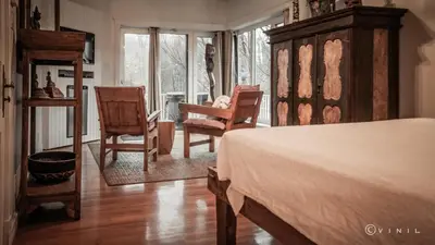 a bedroom with a bed and two chairs and windows at Villa Nao in Roxton Falls