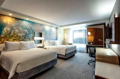 a hotel room with two beds and a desk at Courtyard by Marriott Montreal West Island/Baie D’Urfe in Baie-dʼUrfé