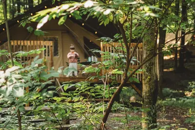 a young boy standing in front of a wooden house at Huttopia Sutton in Sutton