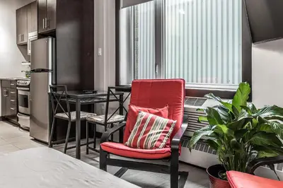 a living room with a red chair and a kitchen at Cjour Apartments in Montréal
