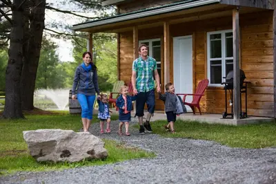 a man and a woman and two children walking in front of a cabin at Chalets du Domaine Yamaska in Bromont