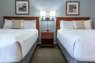 two beds in a hotel room with white sheets at Hôtel Saint-Laurent Montréal in Montréal