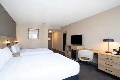 a hotel room with two beds and a desk and a television at Sandman Hotel Montreal - Longueuil in Longueuil