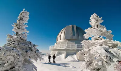 two people skiing in the snow in front of an observatory at Aux Retrouvailles spa à l'année in Lac-Mégantic