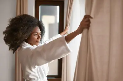 a woman in a white shirt opening a curtain at Holiday Inn Hotel & Suites - Montreal Centre-ville Ouest by IHG in Montréal