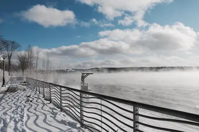 a fence next to a body of water with snow at Maison du lac in Lac-Mégantic