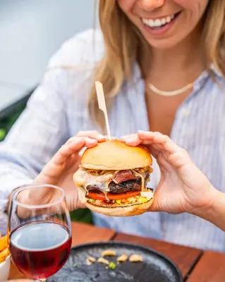 a woman holding a sandwich with a glass of wine at Montreal Marriott Chateau Champlain in Montréal