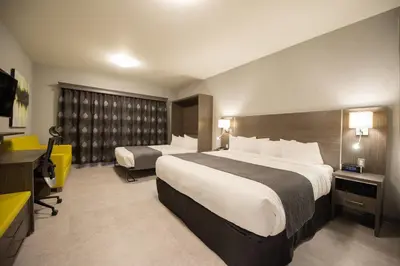 a hotel room with two beds and a desk at Hotel & Suites Le Dauphin Drummondville in Drummondville