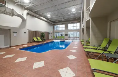 a pool in a room with green chairs and a pool at Hotel & Suites Le Dauphin Drummondville in Drummondville