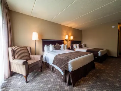 a hotel room with two beds and a chair at Le President Sherbrooke in Sherbrooke