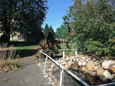 a fence around a pond with rocks and trees at MHotel Domaine l'Envolée- Maison Fleurie in Victoriaville