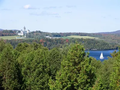 a house on a hill with a boat in the water at La Belle Victorienne in Magog-Orford