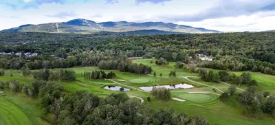 an aerial view of a golf course with mountains in the background at Manoir Des Sables, an Ascend Collection Hotel in Magog-Orford