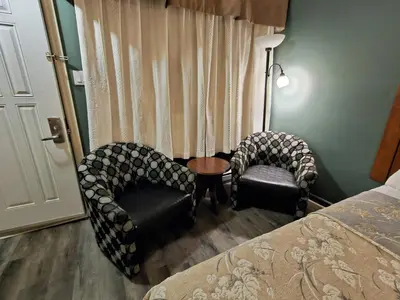 a bedroom with two chairs and a bed and a window at Hotel-Motel Drummond in Drummondville