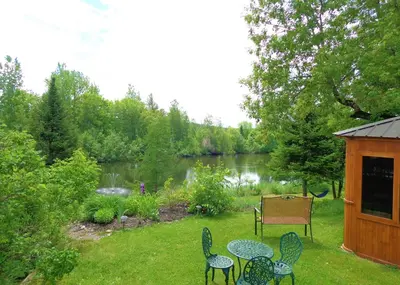 a yard with chairs and a table and a lake at Motel des Deux Lacs in Waterloo