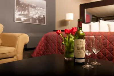 a bottle of wine and two glasses on a table with flowers at Hotel L'Express in Longueuil