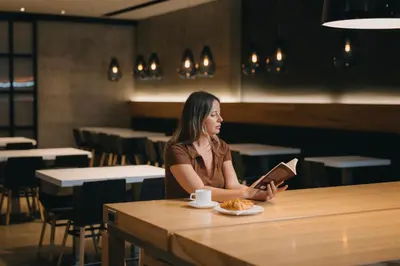 a woman sitting at a table reading a book at Le Dauphin Montréal Centre-Ville in Montréal