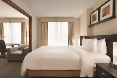 a hotel room with a large white bed and a chair at Embassy Suites by Hilton - Montreal in Montréal