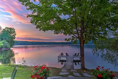a dock on a lake with a tree and a sunset at Ripplecove Hotel & Spa in Ayer's Cliff