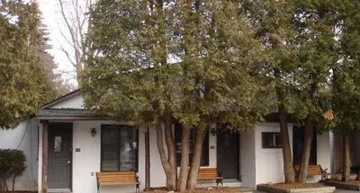 a white house with trees in front of it at Chalet Beaconsfield Motel in Beaconsfield