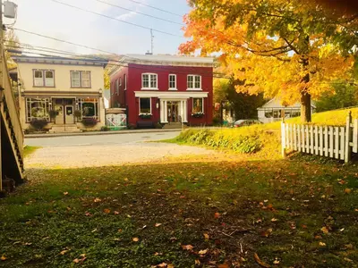 a street with a red house and a white fence at Suites North Hatley in North Hatley