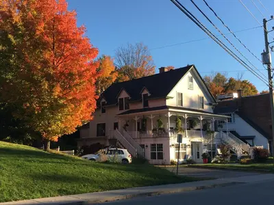 a white house with a porch on a street at Suites North Hatley in North Hatley