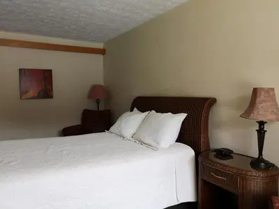 a bedroom with a bed with white sheets and a lamp at Hotellerie Jardins de Ville in Sherbrooke