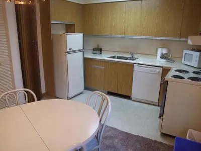 a kitchen with a table and a white refrigerator at Hotellerie Jardins de Ville in Sherbrooke