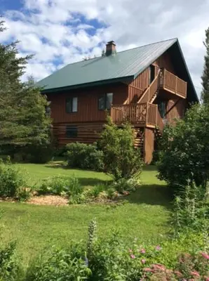 a large wooden house with a balcony in the yard at La Maison Pamaljolie in Ayer's Cliff