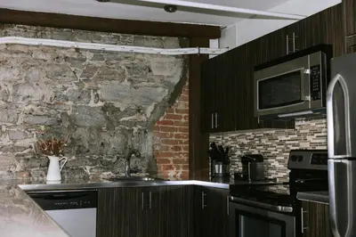a kitchen with black cabinets and a stone wall at Lofts du Vieux-Port by Gray Collection in Montréal