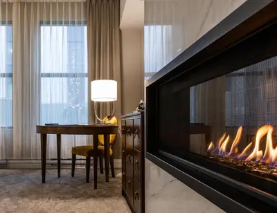 a fireplace in a hotel room with a desk and a table with a fire at Hôtel Birks Montréal in Montréal