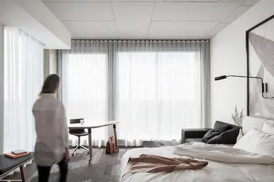 a woman walking through a bedroom with a bed and a desk at Hôtel Escad Quartier DIX30 in Brossard