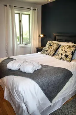 a bedroom with a bed with white sheets and a window at Domaine Jolivent in Lac-Brome