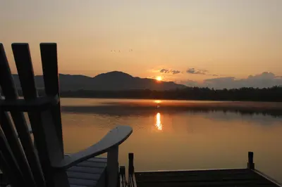 a chair sitting on a dock in front of a lake at La Maison Jaune D'Eastman in Eastman