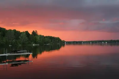 a sunset over a lake with a dock on the water at La Maison Jaune D'Eastman in Eastman