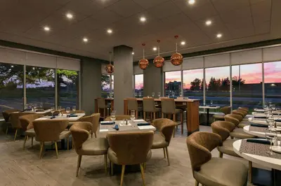 a restaurant with tables and chairs and large windows at Embassy Suites By Hilton Montreal Airport in Pointe-Claire