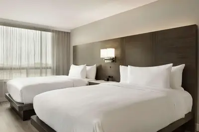 two beds in a hotel room with white sheets at Embassy Suites By Hilton Montreal Airport in Pointe-Claire