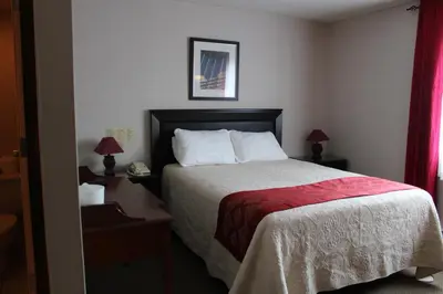 a bedroom with a bed with a red blanket and two lamps at Motel Capri & Suites in Repentigny