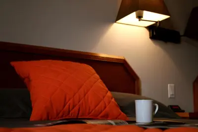 a bed with an orange pillow and a lamp at Hôtel Val-des-Sources in Asbestos