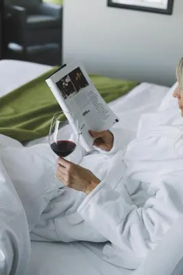 a woman laying in bed with a book and a glass of wine at Hôtel Rive Gauche in Beloeil Village