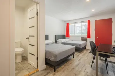 a bedroom with two beds and a desk and a table at Motel Champlain in Brossard