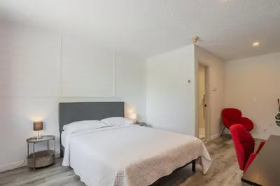 a bedroom with a white bed and a red chair at Motel Champlain in Brossard