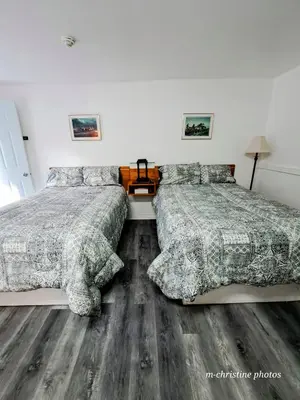 two beds in a bedroom with wooden floors at Motel Bonsoir in Joliette