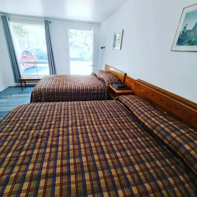 a bedroom with two beds and a plaid blanket at Motel Bonsoir in Joliette