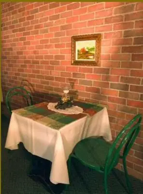 a table with two green chairs next to a brick wall at Auberge - Motel Le Pigeonnier in Farnham