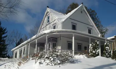 a white house with snow on the ground at Ô Bois Dormant B&B in Magog-Orford