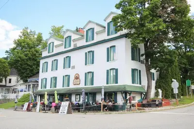 a large white building with people sitting outside of it at Auberge La Chocolatiere in North Hatley