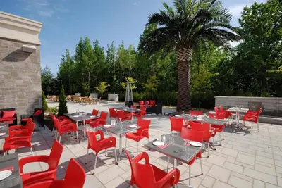 a patio with tables and red chairs and a palm tree at Imperia Hôtel et Suites Terrebonne in Terrebonne
